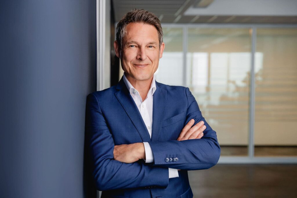 Lockeres Portrait Dr. Oliver Müller, angelehnt an einer blauen Wand